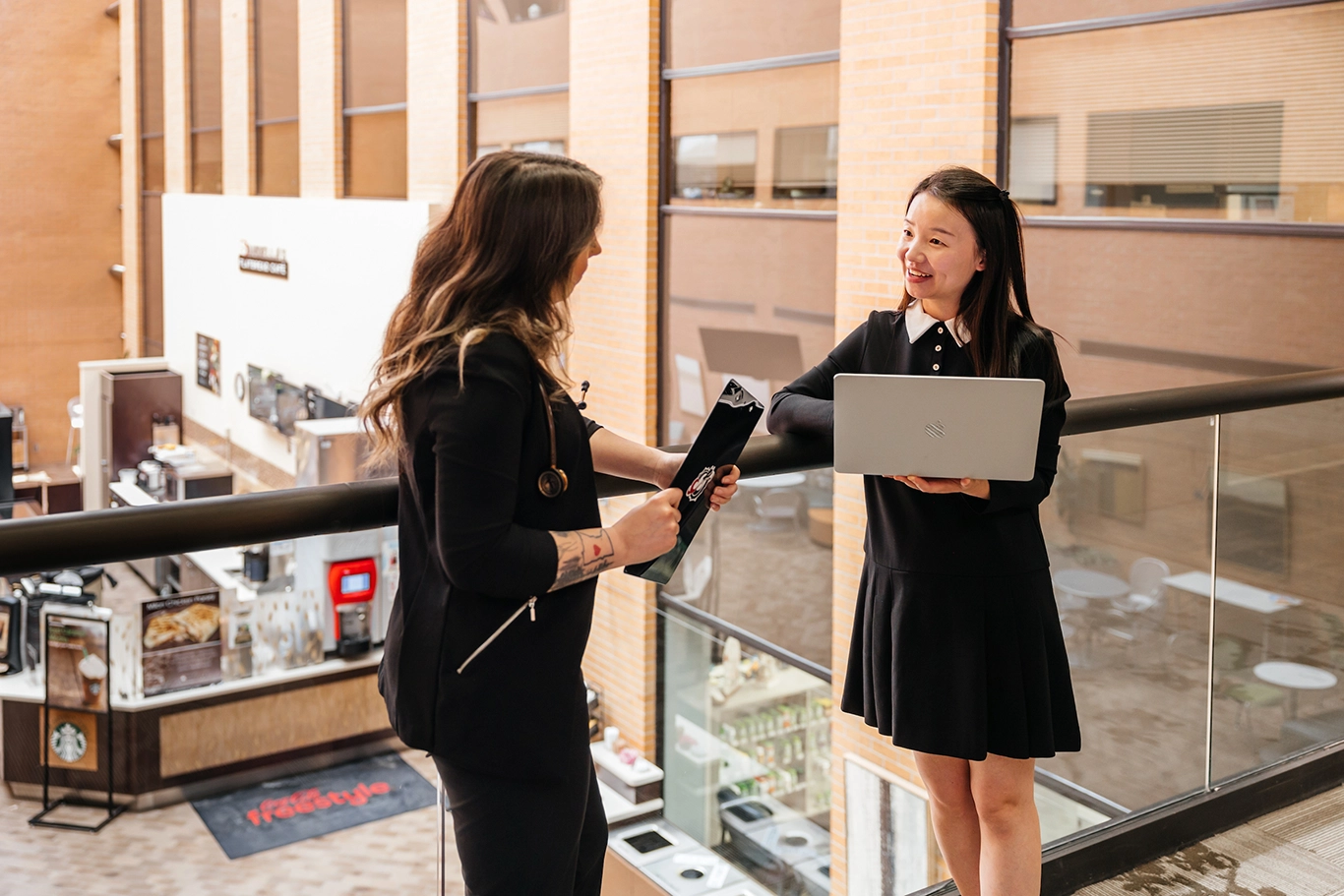 Professor and student talk in skyway of healthcare clinic.