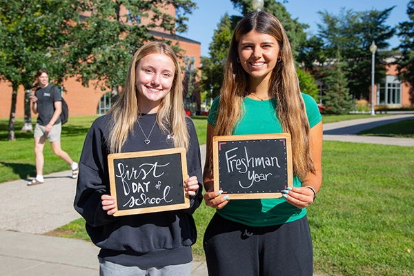 Two students holding chalkboard sign, one says first day of school the other says freshman year