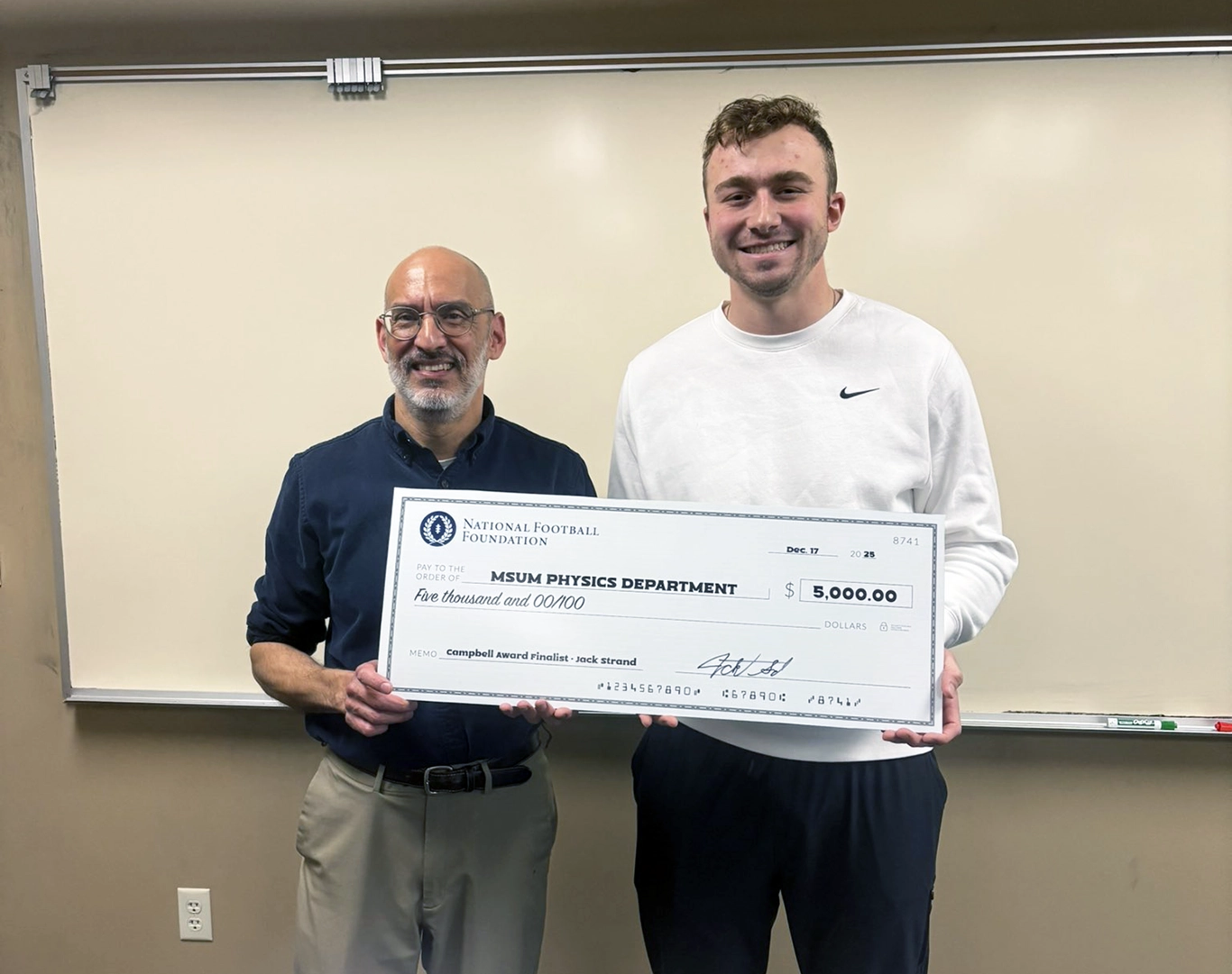 Jack Strand hands Dr. Shastri a check from the National Football Foundation.